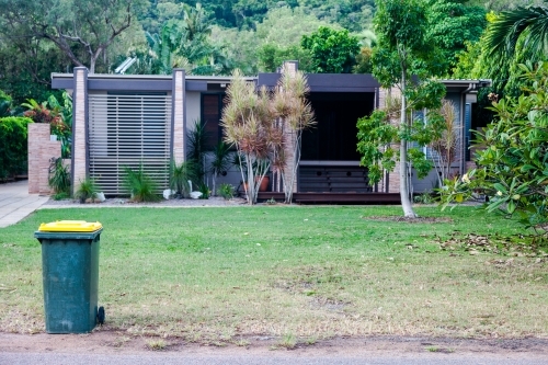 horizontal shot of a house with trees, grass and a trash bin in front