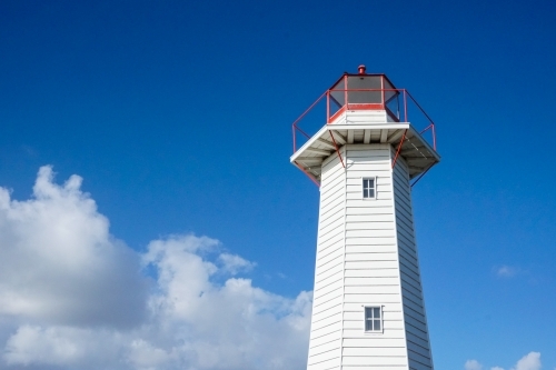horizontal shot of a lighthouse with white clouds and blue skies in the background on a sunny day