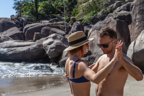 horizontal shot of a man and woman dancing in the beach with rocks in the background on a sunny day - Australian Stock Image