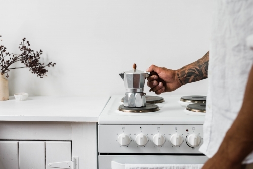Horizontal shot of a man's hand holding a coffee maker on a stovetop burner