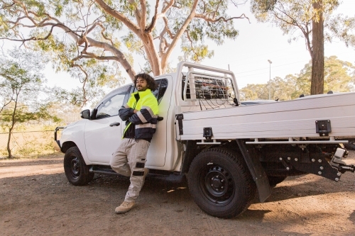 horizontal shot of a man with curly hair wearing neon jacket standing against a white pick up truck - Australian Stock Image