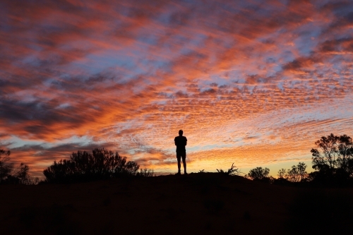 silhouetted person standing on a hilltop at sunset.