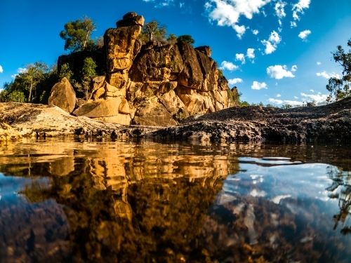 Horizontal shot of a reflection of rocks in water on a cloudy blue sky