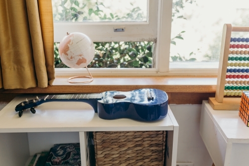 Horizontal shot of a room painted mostly in white with blue ukulele, and a globe near the window - Australian Stock Image