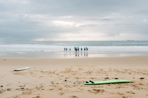 horizontal shot of a shoreline with two surfboards and nine people standing on the sea water