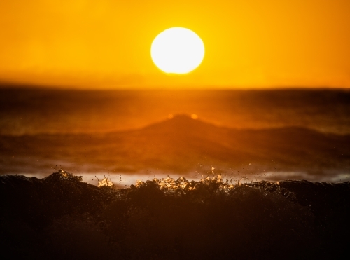 Horizontal shot of a sun above the ocean waves crashing into the water at sunrise - Australian Stock Image