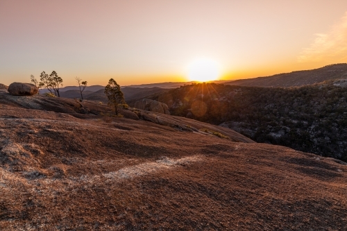 horizontal shot of a sunset on a mountain top with rock, trees and bushes