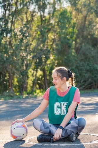 horizontal shot of a young woman sitting on the ground looking at her hand on top of a net ball - Australian Stock Image