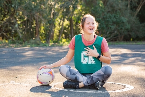 horizontal shot of a young woman sitting on the ground with one hand placed on top of a net ball - Australian Stock Image