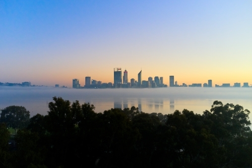 Perth skyline at dawn with fog on the Swan River and silhouetted trees