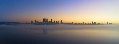 Panoramic shot of Perth skyline at dawn with misty atmosphere and some buildings reflected on water
