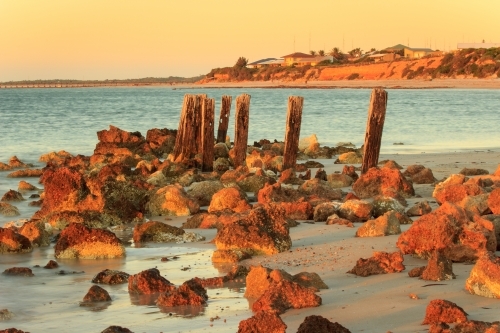 Horizontal shot of rocks and wooden posts on the beach at sunset