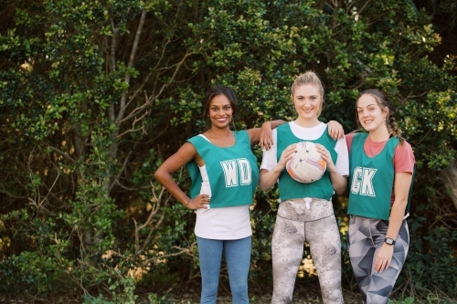 horizontal shot of three young sporty women posing outdoors with one holding a net ball - Australian Stock Image