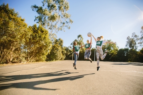 horizontal shot of three young women jumping in mid air on a sunny day with trees in the background - Australian Stock Image
