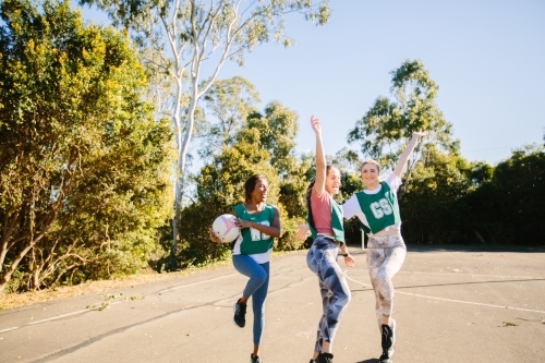 horizontal shot of three young women with arms raised up high playing net ball on a sunny day - Australian Stock Image