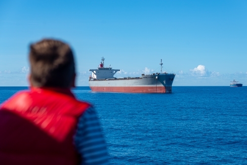 Horizontal shot of two cargo ships sailing with a person looking at them