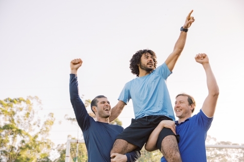 horizontal shot of two men carrying a man on their shoulders while raising their arms up high - Australian Stock Image