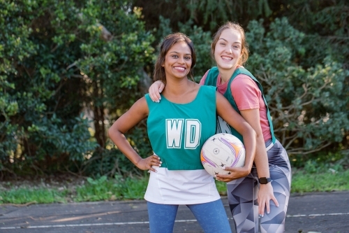 horizontal shot of two young women posing while one holding a netball - Australian Stock Image