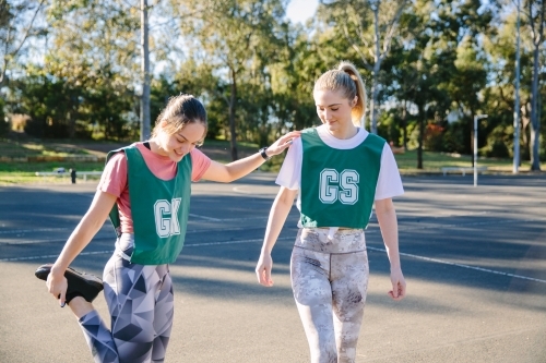 horizontal shot of two young women with one stretching her leg while holding on the shoulder - Australian Stock Image