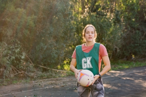 horizontal shot of young woman in sports clothes holding a net ball with two hands on a sunny day - Australian Stock Image