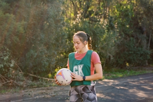 horizontal shot of young woman in sports clothes holding a net ball with two hands on a sunny day - Australian Stock Image