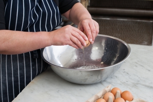 hospitality worker breaking eggs into a bowl - Australian Stock Image