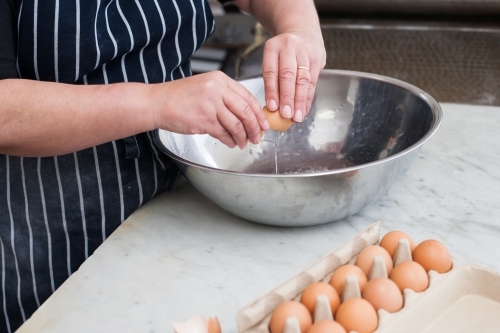 hospitality worker breaking eggs into a bowl - Australian Stock Image
