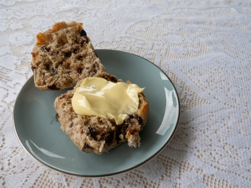 Hot cross bun with butter on a blue plate with lace table cloth - Australian Stock Image