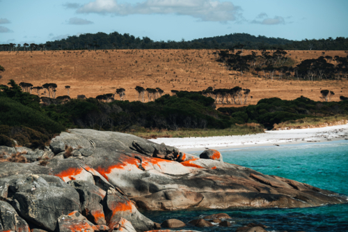 Huge reddish rocks along the shoreline with blue waters. - Australian Stock Image