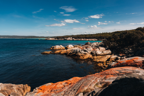 Huge reddish rocks along the shoreline with blue waters - Australian Stock Image