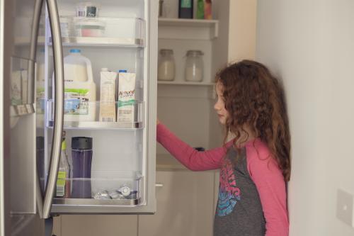 Hungry growing girl looking for food in fridge - Australian Stock Image