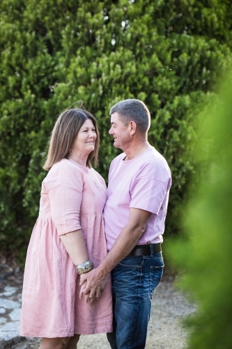 Husband and wife couple standing holding hands smiling at each other - Australian Stock Image