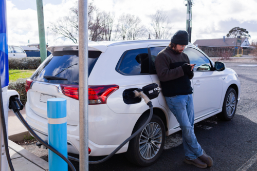 Hybrid ev car charging at public charger in carpark with man waiting beside vehicle  - Australian Stock Image
