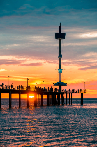 Iconic Brighton jetty with people silhouettes at sunset. - Australian Stock Image