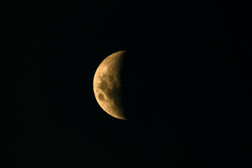 Illuminated moon surface showing visible craters and rugged textures against the black night sky - Australian Stock Image