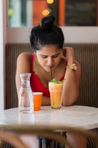 indian woman in a cafe, drinking a juice - Australian Stock Image