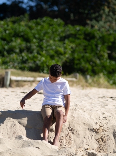 Indigenous boy playing on a sand ledge - Australian Stock Image