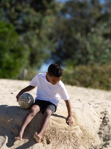 Indigenous boy playing on a sand ledge with ball - Australian Stock Image