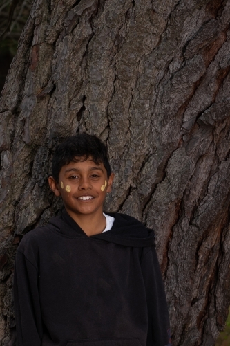 Indigenous boy standing near an old tree trunk