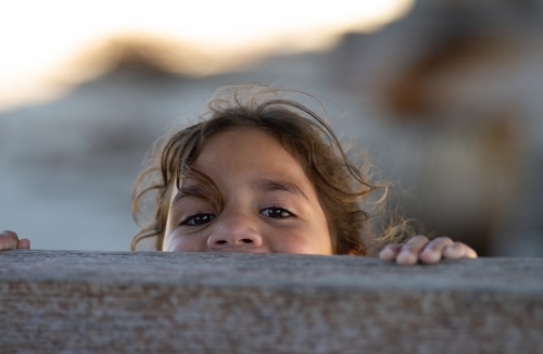 Indigenous girl peeping over wooden fence - Australian Stock Image