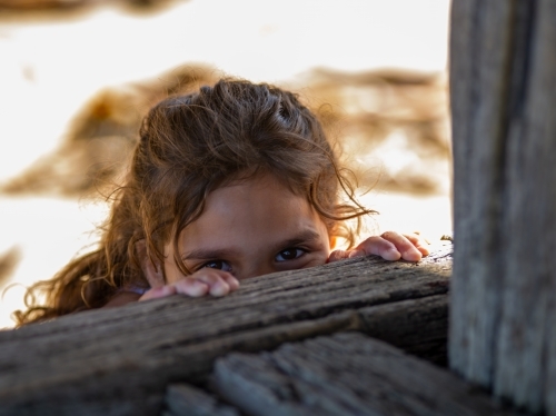 Indigenous girl peeping over wooden fence