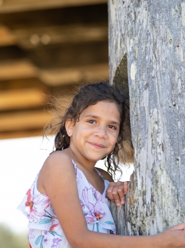 Indigenous girl standing against a wooden pole - Australian Stock Image