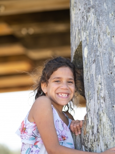 Indigenous girl standing against a wooden pole - Australian Stock Image