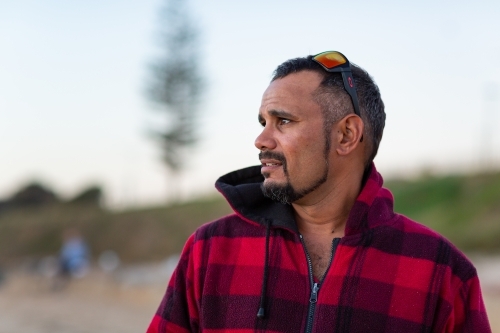 Indigenous man gazing out of frame with sunnies on head - Australian Stock Image