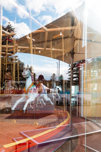 Indoor carousel behind rounded glass window with reflection of outdoors in Glenelg South Australia - Australian Stock Image
