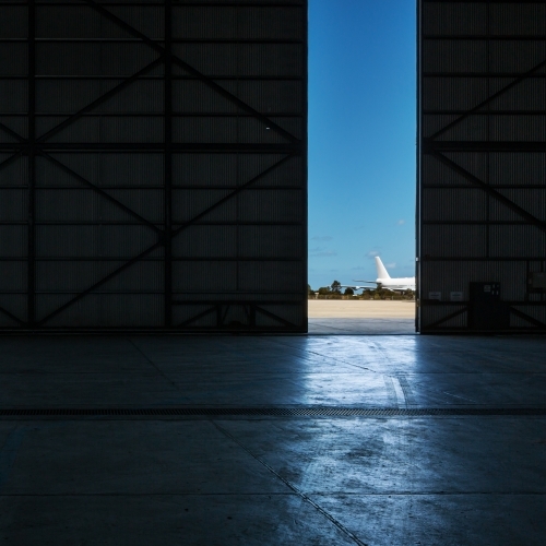 Inside an airport hangar looking out to a plane on the runway through a narrow opening - Australian Stock Image