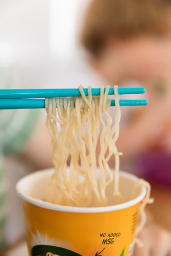 instant ramen noodles being lifted from a paper cup using chopsticks - Australian Stock Image