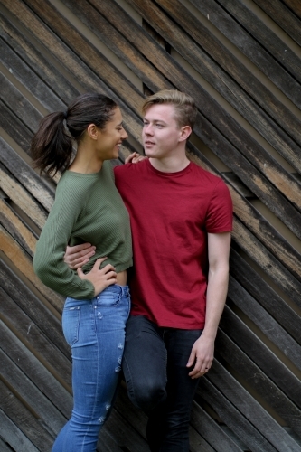 Interracial couple chatting whilst leaning up against a wooden panelled wall - Australian Stock Image