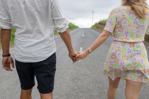 Interracial couple holding hands while walking on a road - Australian Stock Image