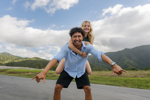 Interracial couple laughing during piggyback ride on a country road - Australian Stock Image